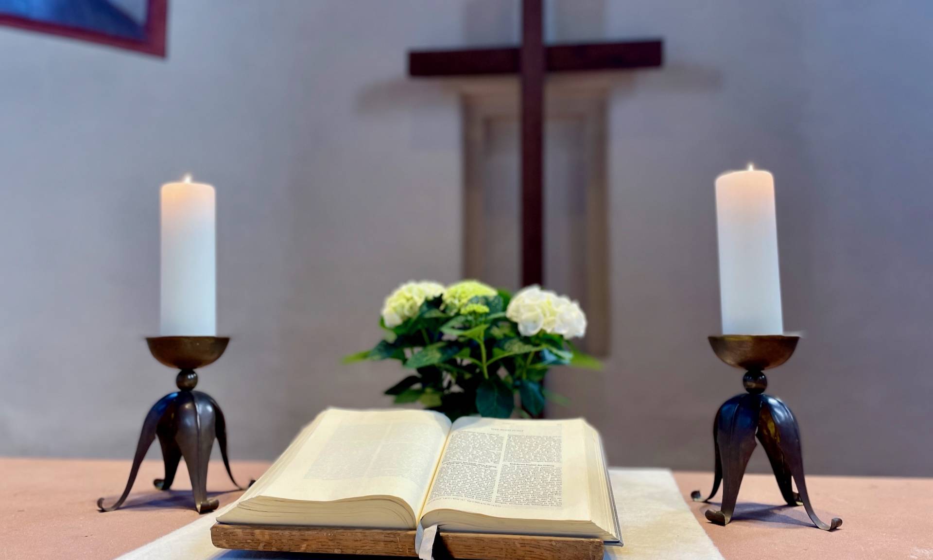 Altar mit Bibel, Kerzen und Kreuz im Hintergrund